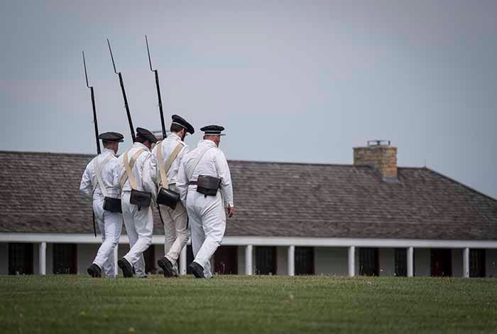 Historical re-enactors march in the parade ground in white outfits with bayonets 