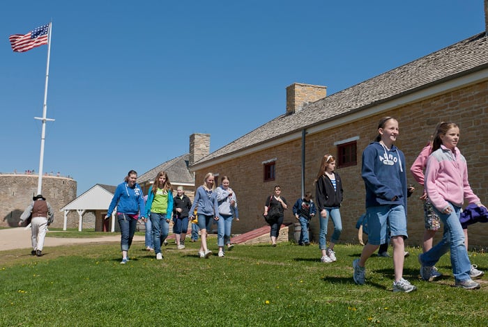 A group of middle school-age children walk along the front of a building at Fort Snelling 